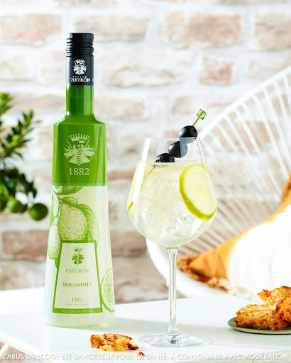 Bouteille de liqueur de bergamote Joseph Cartron avec un verre de cocktails.